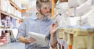 Young man shopping or working in a hardware warehouse standing checking supplies on his tablet