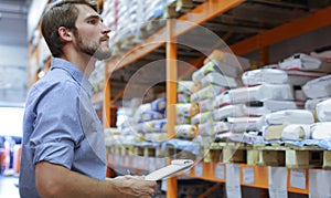 Young man shopping or working in a hardware warehouse standing checking supplies on his tablet