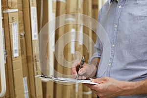 Young man shopping or working in a hardware warehouse standing checking supplies on his tablet