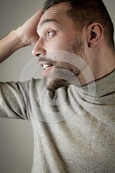 Young man with a short beard in profile with his hand on his head looks surprised