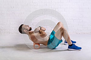 A young man in shorts is doing exercises on a foam roller on his back