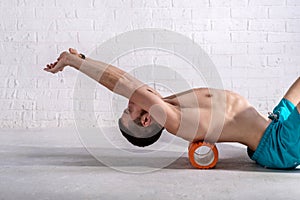 A young man in shorts is doing exercises on a foam roller on his back