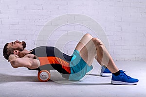 A young man in shorts is doing exercises on a foam roller on his back