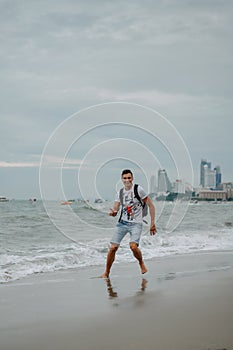 A young man in shorts and a t-shirt is having fun and actively playing with the sea. Running, jumping and having fun at