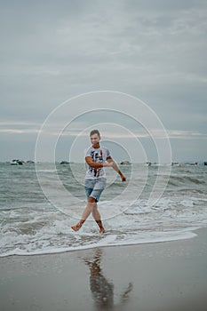 A young man in shorts and a t-shirt is having fun and actively playing with the sea. Running, jumping and having fun at