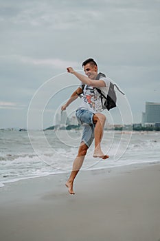 A young man in shorts and a t-shirt is having fun and actively playing with the sea. Running, jumping and having fun at