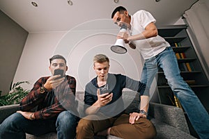 Young man shouting through a loudspeaker at friends which using a mobile phone