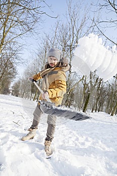 Young man shoveling snow near a small wood