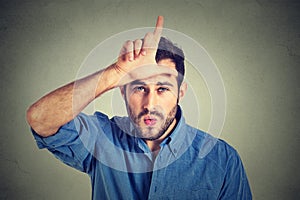 Young man showing loser sign on forehead, looking at you with disgust photo