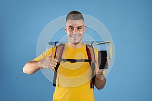 Young man showing mobile phone with empty screen and making thumb up on blue background. Space for design