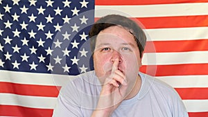 Young man showing silence gesture on the background of an USA flag
