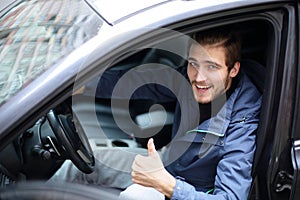 Young man showing thumb up,sitting at the wheel of a new car