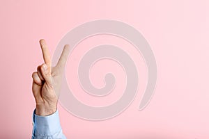 Young man showing victory gesture on color background