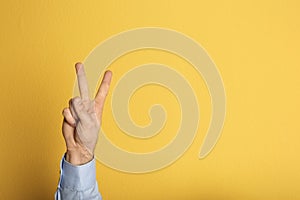 Young man showing victory gesture on color background