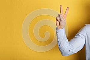 Young man showing victory gesture on color background.