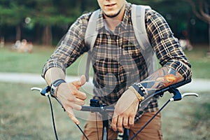 Young Man Shows A Hang Loose Shaka Surfer Sign By Hand Sitting On A Bicycle On Green Summer Meadow