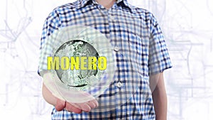 Young man shows a hologram of the planet Earth and text Monero