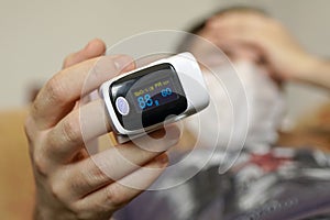 young man is sick with COVID-19 coronavirus and measures oxygen saturation at home on the couch. Pulse Oximeter portable