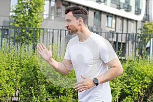 A young man sideways view has jogging or race walking in a modern residential area with buildings and parkland on a