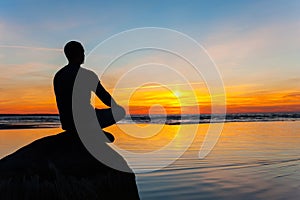 Man silhouette sitting on stone at the seaside contemplating sun