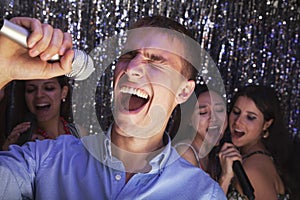 Young man singing into a microphone at karaoke, friends singing in the background