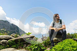 Young man sit in beautiful mountains on hiking trip. Active person resting outdoors in  nature. Backpacker camping outside recreat