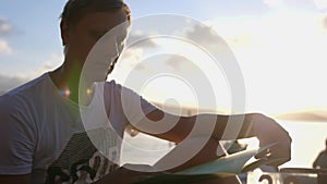 Young man sit in a cafe on the beach during sunset, scrolls through the menu. slow motion