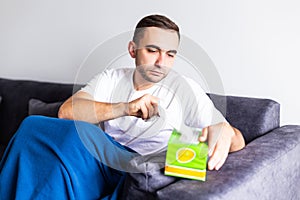 Young man sit on couch feel unwell blowing running nose with napkin at home. Sick male at home have health problems, get flu or