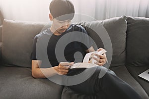 Young man sit down on the sofa reading book at home