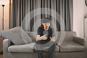 Young man sit down on the sofa while using mobile phone and drink coffee  relaxing at home
