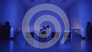 A young man sits alone on an empty dance floors and uses laptop to invite friends to a party