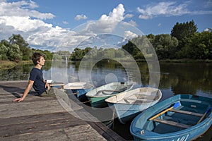 A young man sits on a boat dock on a bright summer day