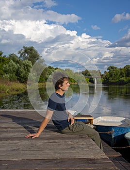 A young man sits on a boat dock on a bright summer day