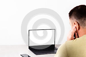 A young man sits in front of a laptop with a white mockup on the screen