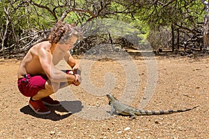 Young man sits with green iguana in nature