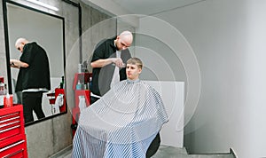 Young man sits in a hairdresser`s chair and cuts hair at a professional hairdresser, barber uses a clipper to create stylish