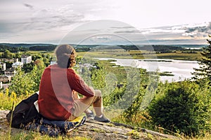 A young man sits on a hill and enjoys nature and the sunset. Beautiful landscape