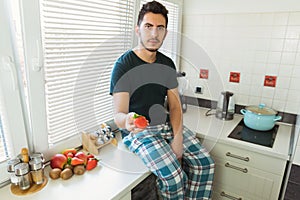 A young man sits in the kitchen and holds ripe strawberries in his hands
