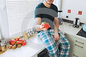 A young man sits in the kitchen and holds ripe strawberries in his hands