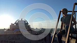 Young man sits on a metallic platform on a high building in summer.