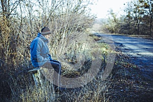 A young man sits on an old bench at a rural bus stop in autumn