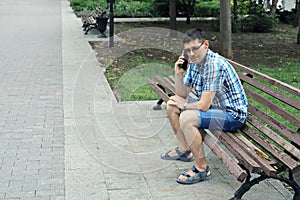 Young man sits on park bench and calls on the phone