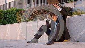 Young man sits on the pavement and strikes his briefcase after getting fired.