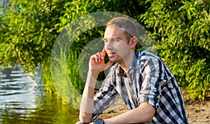 A young man sits by the river and looks thoughtfully into the distance