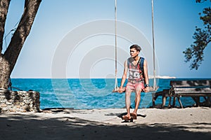 Young man sits on a rope swing on the beach on Ko Samet