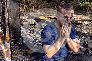 Young man sits on the ruins of house destroyed with fire.