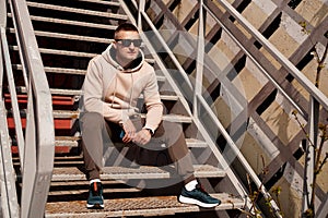 A young man sits on the steps in the city. Urban style. Lifestyle photo