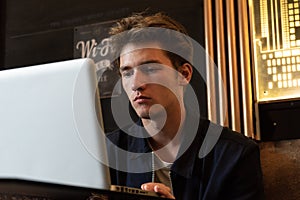 Young man sits at a table in front of a laptop. man working