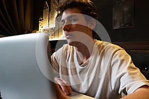 Young man sits at a table in front of a laptop.