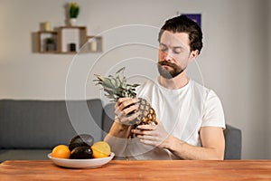 A young man sits at a table and talks about the usefulness of fruits, he picks them up and shows pineapple. Healthy food